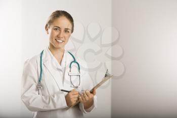 Royalty Free Photo of a Female Doctor Writing on a Clipboard, Smiling and Looking at Viewer
