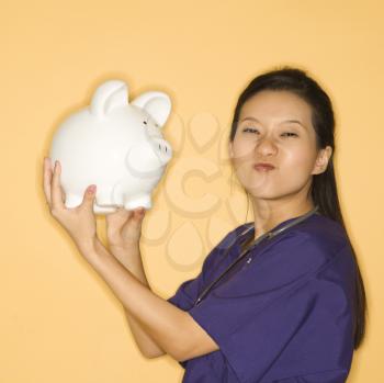 Royalty Free Photo of a Doctor Holding a Piggy Bank and Scrunching Her Nose 