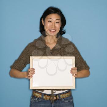 Pretty Asian mid adult woman holding blank sign on blue background.