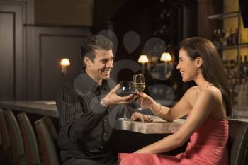 Royalty Free Photo of a Couple at a Bar Toasting Wine Glasses and Smiling