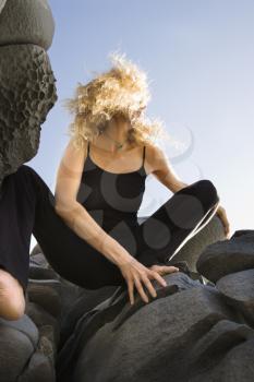 Royalty Free Photo of a Woman Crouching on Rocks With Hair Blowing Wildly in the Wind