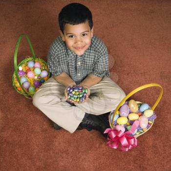Royalty Free Photo of a Boy Sitting on the Floor With Two Easter Baskets Holding Chocolate Eggs in His Hands