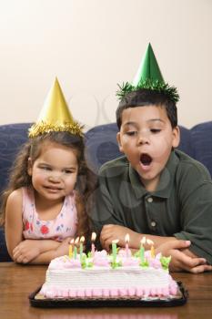 Royalty Free Photo of a Girl and Boy Wearing Party Hats Preparing to Blow Candles Out on a Birthday Cake