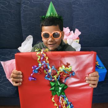 Royalty Free Photo of a Boy Wearing a Party Hat and Sunglasses Holding a Large Birthday Present and Smiling