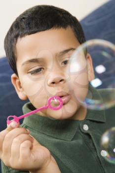 Hispanic boy blowing large soap bubbles.