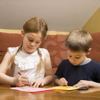 Caucasian boy and girl drawing on paper with crayons.