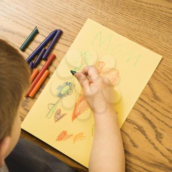 Royalty Free Photo of a Boy Drawing on Yellow Paper With Crayons