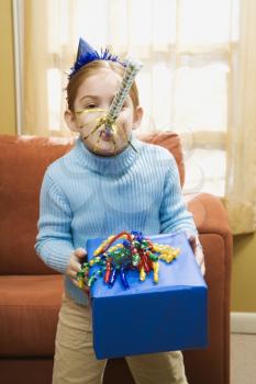 Royalty Free Photo of a Girl Blowing a Noisemaker and Holding a Gift