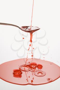 Royalty Free Photo of a Stream of Red Cough Syrup Overflowing Spoon Into a Puddle Below