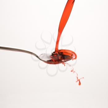 Royalty Free Photo of a Stream of Red Cough Syrup Splashing Out of a Spoon