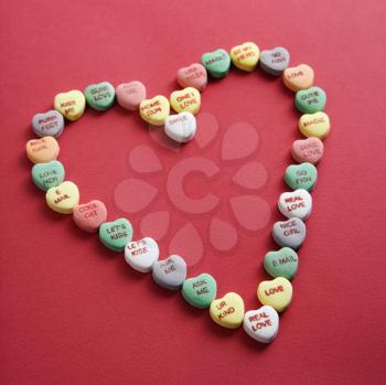 Colorful candy hearts with sayings on them arranged in shape of heart on red background.