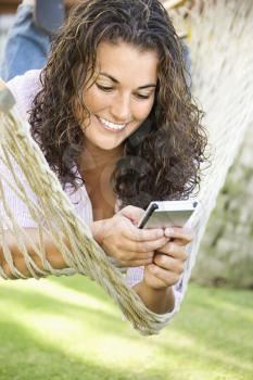 Royalty Free Photo of a Smiling Pretty Woman Lying in a Hammock Using PDA
