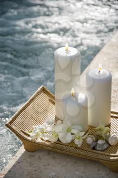 Royalty Free Photo of Lit Pillar Candles on a Tray With White Orchids Beside a Pool