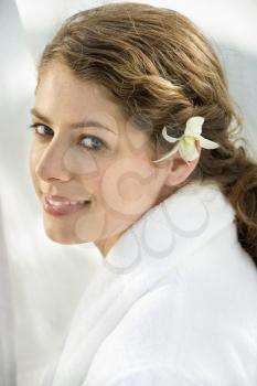 Pretty Caucasian mid-adult woman wearing white terry robe with white orchid flower in hair.