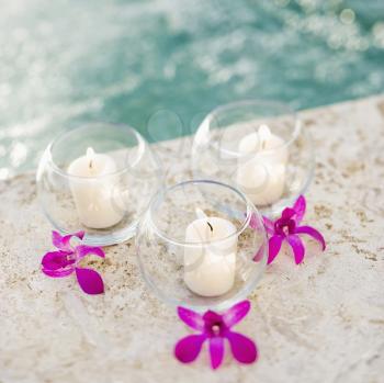 Royalty Free Photo of Three Candles and Three Purple Orchids by a Pool