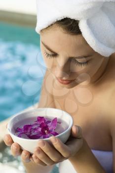 Royalty Free Photo of a Woman Wearing a Towel Around Her Head and Body Holding a Bowl of Purple Orchids Next to a Pool