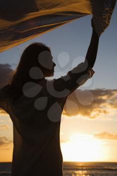 Royalty Free Photo of a Woman Holding Up Fabric in the Breeze Silhouetted By the Sunset