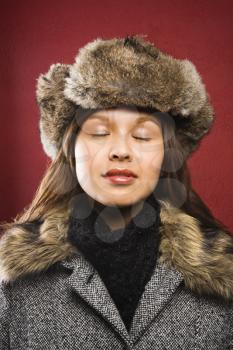 Young adult Caucasian woman wearing fur hat with eyes closed.