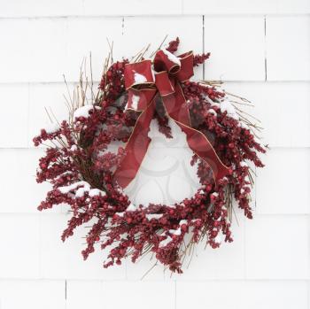 Royalty Free Photo of a Red Wreath Covered in Snow Hanging on a White Brick Wall