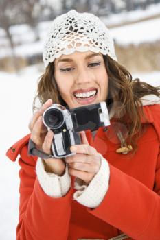 Smiling Caucasian young adult female in winter clothing pointing video camera at viewer.