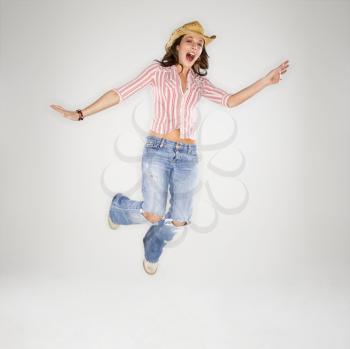 Royalty Free Photo of a Young Woman Wearing a Cowboy Hat Leaping Into the Air With an Excited Expression