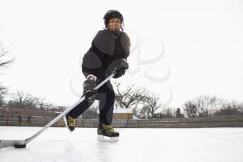 Royalty Free Photo of a Boy in an Ice Hockey Uniform Skating on an Ice Rink Moving Puck