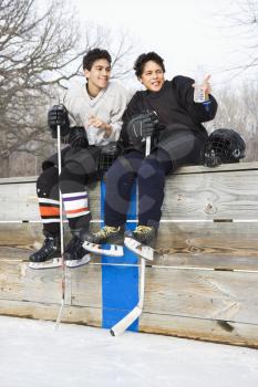 Royalty Free Photo of Two Boys in Ice Hockey Uniforms Holding a Hockey Sticks Sitting on the Sidelines