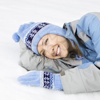 Attractive smiling mid adult Caucasian woman wearing blue ski clothing lying in snow looking at viewer.