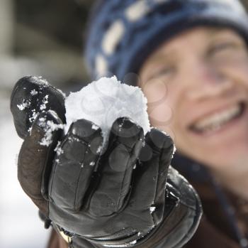 Caucasian male teenager holding snowball out towards viewer.