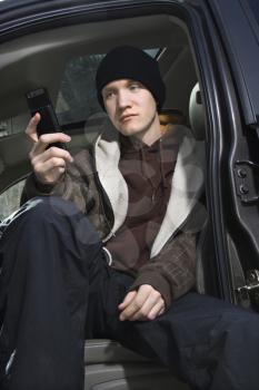 Royalty Free Photo of a Male Teenager Sitting in a Car Looking at a Cellphone