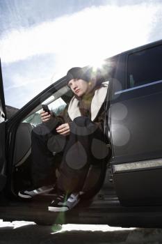Royalty Free Photo of a Male Teenager Sitting in a Car Looking at a Cellphone
