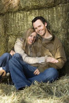 Royalty Free Photo of a Couple Sitting on Hay Hugging and Smiling