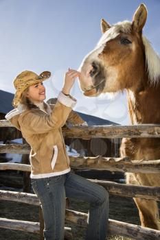 Royalty Free Photo of a Woman Leaning on a Fence Petting a Horse
