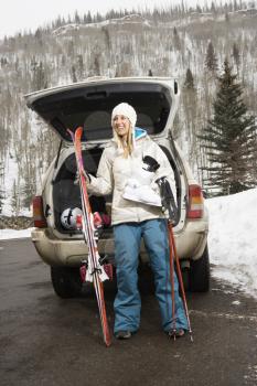 Royalty Free Photo of a Woman Holding Ski Equipment and Smiling by an Automobile