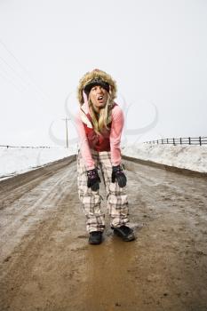 Royalty Free Photo of a Woman in Winter Clothes Standing Alone in the Middle of a Muddy Dirt Road and Snow Making Strange Facial Expressions