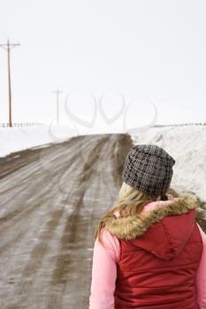 Royalty Free Photo of a Young Woman in Winter Clothes Walking Down a Muddy Dirt Road