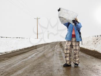 Royalty Free Photo of a Woman in Winter Clothes Standing on a Muddy Dirt Road Holding an Open Map 