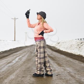 Royalty Free Photo of a Young Woman in Winter Clothes Standing on a Muddy Dirt Road Looking at a Cellphone