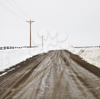 Royalty Free Photo of a Muddy Dirt Road in Rural, Snow Covered Landscape with Power Lines