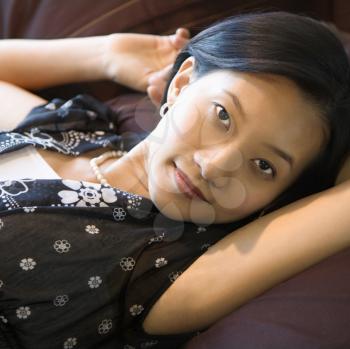 Portrait of Asian female lying on bed looking at viewer.