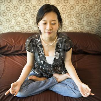 Asian female sitting on bed meditating.
