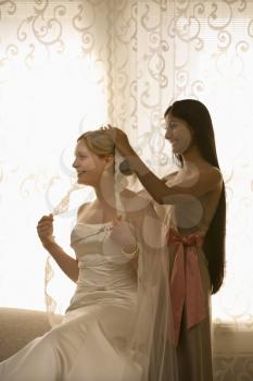 Royalty Free Photo of a Bridesmaid Placing a Veil on a Bride