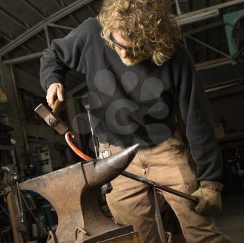 Royalty Free Photo of a Metal Smith Shaping Metal on an Anvil