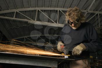 Caucasian male metalsmith shaping metal and creating sparks.