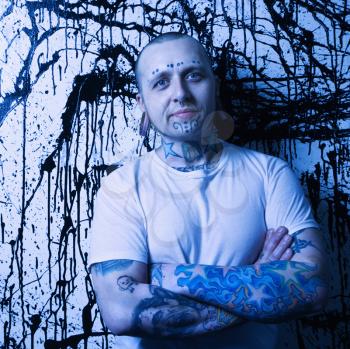 Royalty Free Photo of a Tattooed and Pierced Man Standing Against a Paint Splattered Background