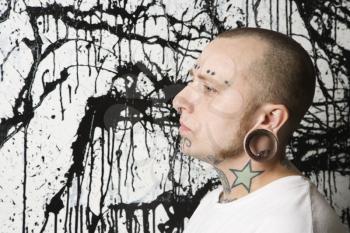 Royalty Free Photo of a Tattooed and Pierced Man Against a Paint Splattered Background