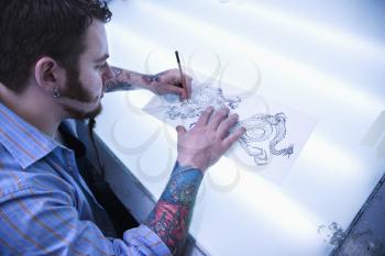 Royalty Free Photo of a Male Tattoo Artist Drawing a Tattoo on a Light Table