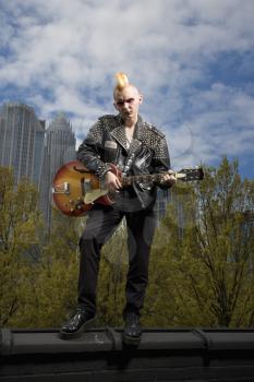 Royalty Free Photo of a Punk Holding a Guitar With the Skyline in the Background