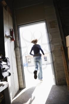 Royalty Free Photo of a Woman Running Through an Open Door From a Building to Sunny Outside