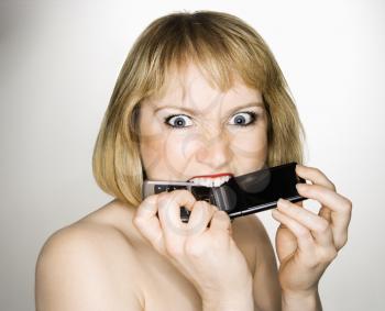 Portrait of young blonde caucasian woman who is biting her cellphone angrily.